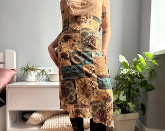 May include: A tan patchwork dress with a square neckline and spaghetti straps. The dress features a mix of floral and geometric patterns in shades of brown, teal, and beige. The dress is knee-length and has a slightly asymmetrical hemline.