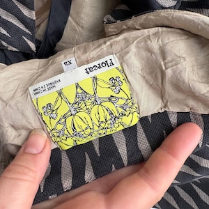 May include: Close-up of a garment tag with the brand name "Floreat" in white on a yellow background. The tag features a floral design and the text "MADE IN CHINA FABRIQUE EN CHINE". The garment is XS size.