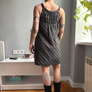 May include: A black and white patterned dress with thin straps. The dress has a diamond-like design and falls to the mid-thigh. The model is wearing black boots. The dress is a casual summer dress.