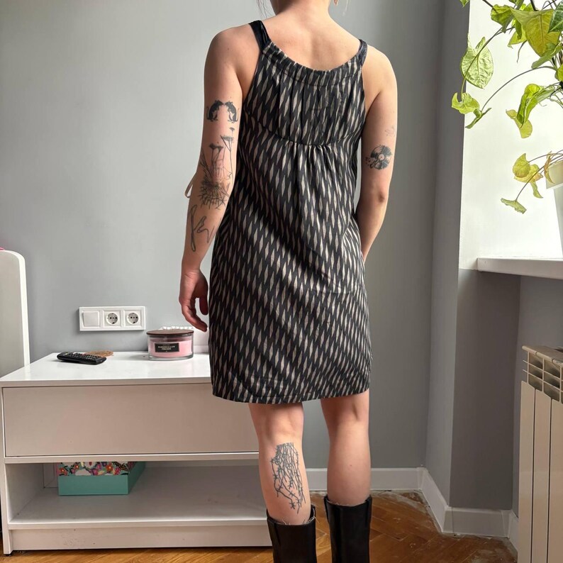 May include: A black and white patterned dress with thin straps. The dress has a diamond-like design and falls to the mid-thigh. The model is wearing black boots. The dress is a casual summer dress.
