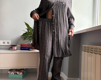 May include: A two-piece set of vertically striped clothing in shades of brown, gray, and purple. The set includes a long-sleeved button-down shirt and matching pants. The shirt is open, revealing the midriff. The outfit is worn with black boots.