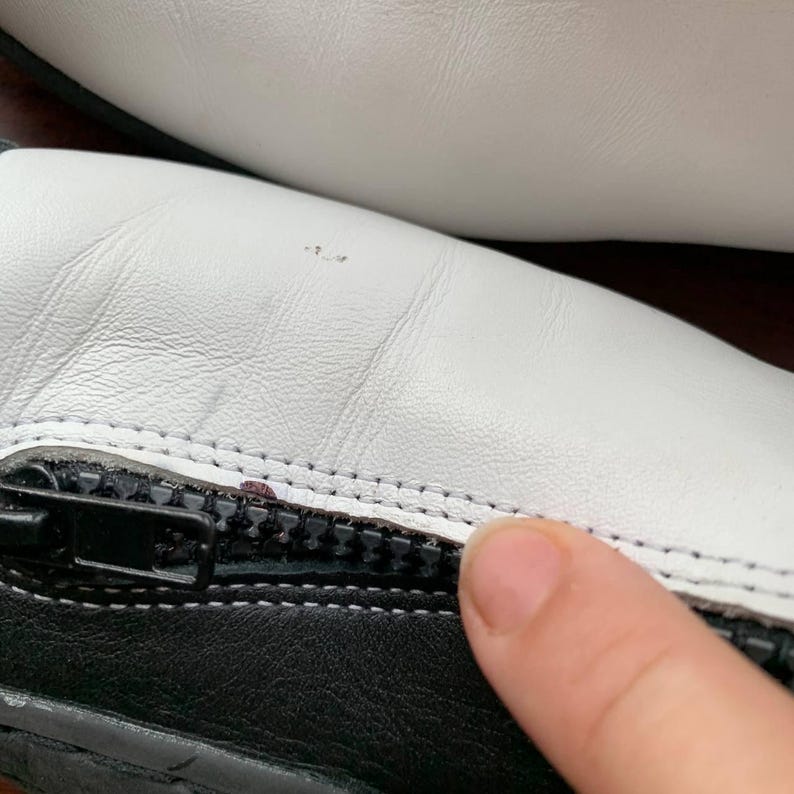 Puede incluir: Primer plano de un zapato blanco y negro con un detalle de cremallera. El zapato es de cuero y tiene una suela blanca.