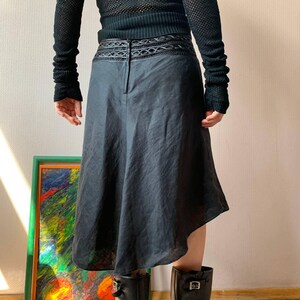 K&ouml;nnte beinhalten: Dunkelgrauer Rock mit asymmetrischem Saum. Der Rock hat einen dekorativen Bund und eine leichte A-Linien-Form. Das Model tr&auml;gt schwarze Stiefel und ein schwarzes Langarm-Oberteil.