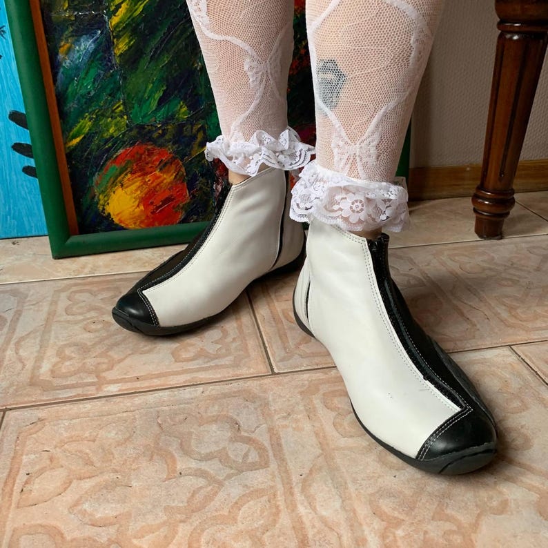 Puede incluir: Botas blancas de tobillo con ribete negro y una cremallera en la parte delantera. Las botas son de cuero y tienen una puntera redonda.