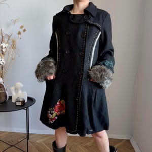 Può includere: Cappotto nero doppiopetto con polsini in ecopelliccia e ricami floreali. Il cappotto presenta dettagli di cuciture bianche e dorate, una gonna svasata e un design unico. Un elegante capo di abbigliamento.