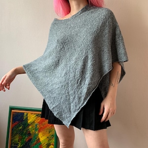 以下が含まれることがあります： ゆったりとしたフィット感と三角形の形状をしたグレーのニットポンチョ。ポンチョは柔らかくふわふわした素材で作られています。