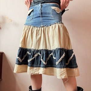 Könnte beinhalten: Ein Jeans- und beiger Rock mit mehrschichtigem Design. Der Rock hat einen Jeansbund mit Taschen und einen Rüschensaum. Der untere Teil des Rocks ist beige, mit einer Jeans- und weißen Spitzenborte.