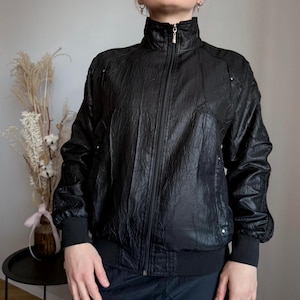 May include: Black Adidas track jacket with a textured, crinkled finish. The jacket has a high collar, full-length zip, and the Adidas logo on the chest. Ribbed cuffs and hem complete the sporty design.