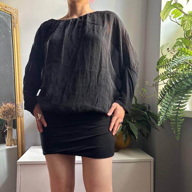 May include: A black long-sleeve blouse with a gathered round neckline and a slightly sheer, textured fabric. The blouse features a loose, draped fit through the torso and sleeves, paired with a solid black, fitted mini skirt with a straight hemline.