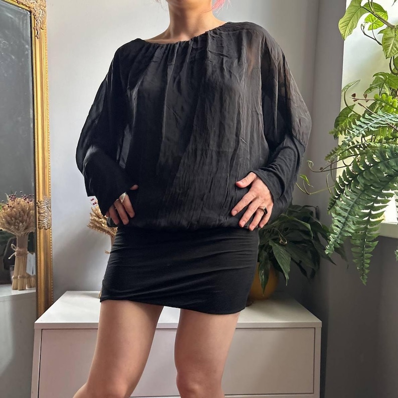 May include: A black long-sleeved blouse featuring a sheer, lightweight fabric with a gathered neckline and a fitted, opaque black mini skirt. The blouse has a loose, draped silhouette with cuffed sleeves, while the skirt sits snugly at the waist.