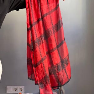 Puede incluir: Una bufanda roja transparente con detalles de encaje negro. La bufanda es rectangular y presenta un patr&oacute;n de rejilla de encaje negro. La tela parece ligera y fluida, adecuada para una variedad de opciones de estilo.