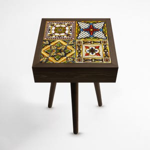 May include: A square side table with a dark brown wooden frame and legs. The tabletop features four decorative ceramic tiles with colorful floral and geometric patterns. The table is approximately 61 cm tall.