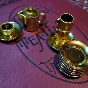 May include: A gold-colored tea set with a teapot, cups, and saucers. The set is on a burgundy surface with the words "The World Tea-Party" printed on it.