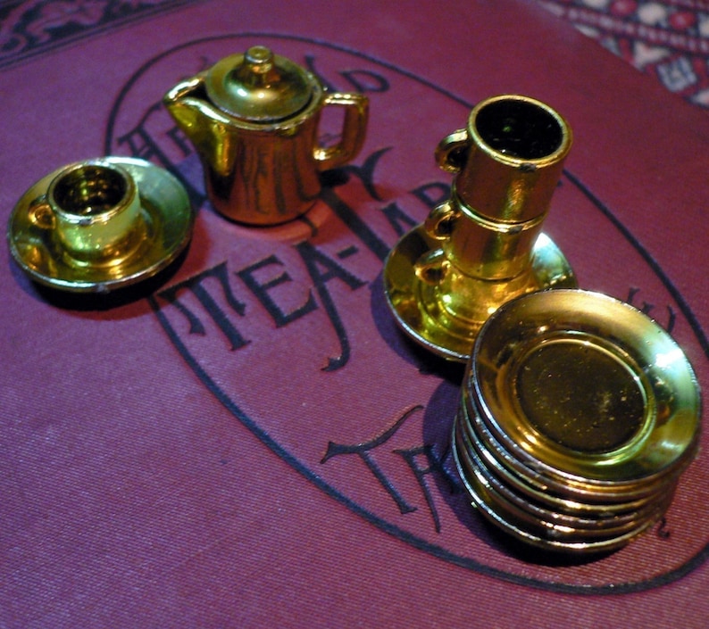 May include: A gold-colored tea set with a teapot, cups, and saucers. The set is on a burgundy surface with the words "The World Tea-Party" printed on it.