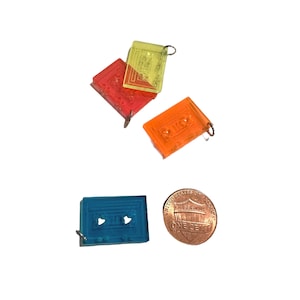 Puede incluir: Tres charms de pl&aacute;stico en forma de casete, uno azul, uno naranja y uno amarillo. Los charms son del tama&ntilde;o de una moneda de un centavo de d&oacute;lar estadounidense.