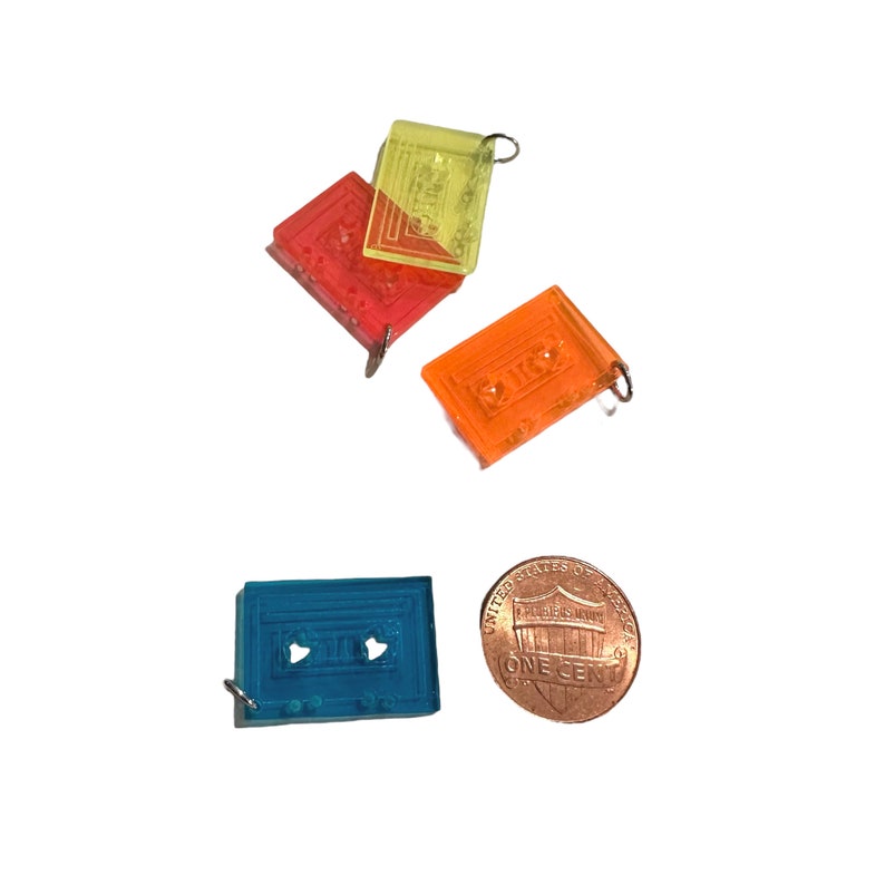 Puede incluir: Tres charms de pl&aacute;stico en forma de casete, uno azul, uno naranja y uno amarillo. Los charms son del tama&ntilde;o de una moneda de un centavo de d&oacute;lar estadounidense.