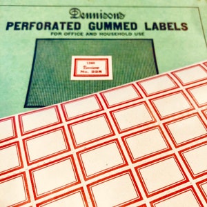 May include: A sheet of perforated gummed labels with red borders. The labels are blank and ready to be used for office or household purposes. The sheet is from Dennison, a company that has been making labels since 1844.