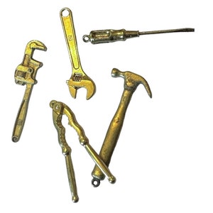 Könnte beinhalten: Ein Satz von fünf goldfarbenen Miniaturwerkzeugen, darunter ein Schraubenschlüssel, ein Hammer, ein Schraubendreher, ein Rohrschlüssel und eine Nussknacker.