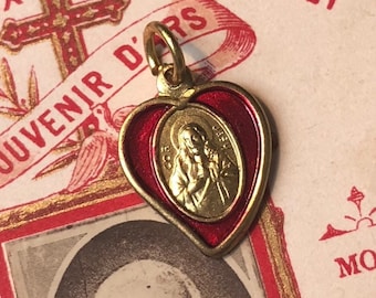 May include: A gold-colored heart-shaped pendant with a red enamel border. The pendant features a depiction of Jesus Christ with a crown of thorns and a heart in his hand. The pendant is inscribed with the words "JESUS" and "COR".