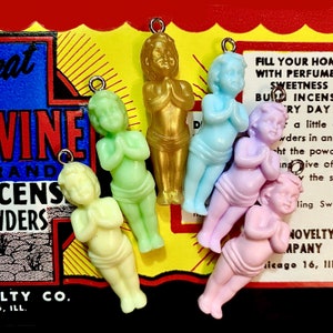 May include: Six small plastic figurines of praying angels in various pastel colors, including light blue, light green, light yellow, and lavender. The angels are all wearing simple dresses and have their hands clasped in prayer. The figurines are hanging from a string and are likely intended as charms or ornaments.