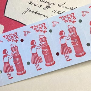 May include: A strip of light blue paper with a repeating red design. The design features a girl in a pleated skirt interacting with a red mailbox. The design also includes birds and leafy branches. The paper has small holes along the edge.
