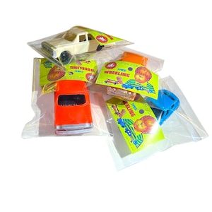 May include: A collection of toy cars in clear plastic packaging. The toys include a cream-colored car, an orange car, and a blue car. Each toy is attached to a yellow and green card with the words "FREE WHEELING" and a cartoon illustration.
