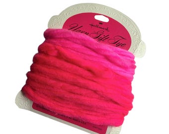 May include: A spool of bright pink yarn gift tie wrapped around a cream-colored cardboard holder. The packaging features the Hallmark logo and the text Yarn Gift Tie in black script. The yarn is a thick, soft, and vibrant fuchsia color.