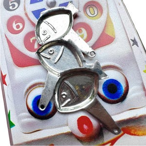 May include: Three silver-colored metal fish-shaped cookie cutters. The cutters are stacked on top of each other. The cutters are on a white surface with a colorful background.
