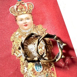 Peut inclure: Deux anneaux dorés à l'aspect épineux. Les anneaux sont entrelacés et sont nets. L'arrière-plan est une image rouge et or d'un enfant portant une couronne.