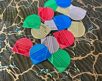 May include: A collection of 12 colourful, metallic game chips with the word "OMEGA" printed on each. The chips are in various shades of red, blue, green, and gold.