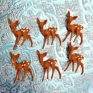 May include: Six brown plastic deer figurines with white spots on a blue and white patterned background.