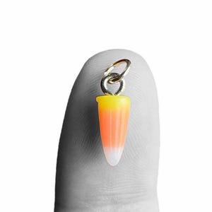 May include: A candy corn charm with a silver-colored loop. The charm features the classic candy corn colors: yellow, orange, and white. The charm is small and detailed, perfect for jewelry making or other crafts.