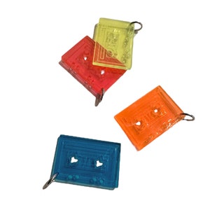 Puede incluir: Tres llaveros de cinta de casete de colores. Uno es amarillo, otro naranja y otro azul.