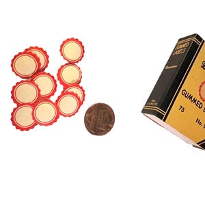 May include: A box of 75 gummed labels with a red and white scalloped edge. The labels are round and have a blank centre. A penny is included for scale.