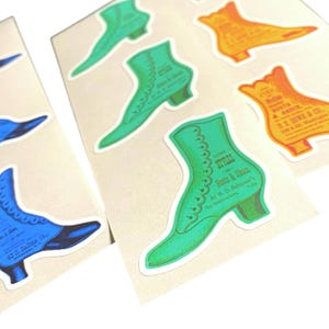 May include: A collection of vintage-style boot stickers in shades of blue, green, and orange. Each sticker features a detailed illustration of a boot with text, including "Boots & Shoes" and "42 S. Salina St."