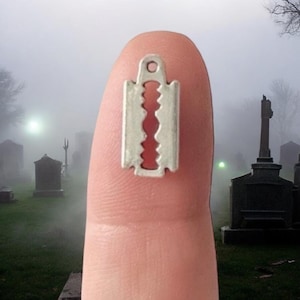 May include: A silver charm shaped like a razor blade, with a small loop at the top for attaching to a necklace or bracelet.