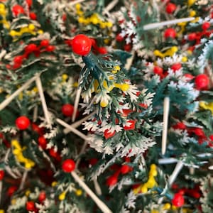 May include: A close-up of a bunch of small artificial Christmas trees with red and yellow berries. The trees are green with white tips and are attached to white toothpicks.