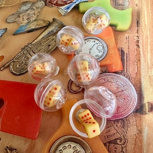 May include: Six clear plastic containers with red and yellow dice inside. The containers are on a wooden surface with a clock face and other decorative elements.