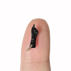 May include: Black keychain charm shaped like a fist with the index finger pointing up. The charm is attached to a gold-colored key ring.