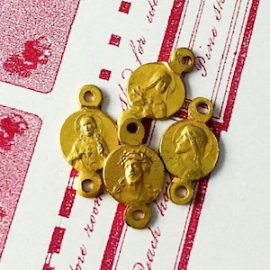 May include: Five gold-toned metal charms with religious figures. Each charm features a different image of Jesus Christ or Mary. The charms have two loops for attaching to a necklace or bracelet.