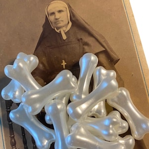 May include: A pile of white plastic bone-shaped beads. The beads are arranged in a random pattern and are all the same size. The beads are in focus, and the background is out of focus.