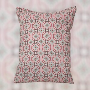 May include: A decorative square pillow with a repeating geometric pattern. The pattern features red, gray, and green shapes on a light pink background. The pillow is a soft, comfortable home decor item.