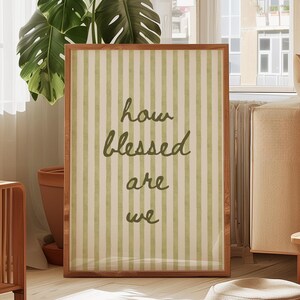 Könnte beinhalten: Ein gerahmter Druck mit einem grün-weiß gestreiften Hintergrund und dem Text "how blessed are we" in brauner Kursivschrift.