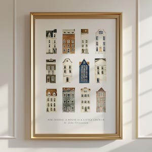 May include: A framed print featuring a watercolor illustration of various buildings. The artwork showcases a collection of colorful houses with unique architectural details. The text at the bottom reads: "FOR INDEED, A HOUSE IS A LITTLE CHURCH St. John Chrysostom."