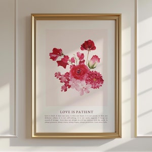 May include: A framed print featuring a watercolour painting of pink and red flowers. The text "LOVE IS PATIENT" is below the flowers. The text reads: "Love is kind, it does not envy, it does not boast, it is not proud. It does not dishonour others, it is not self-seeking, it is not easily angered, it keeps no record of wrongs. Love does not delight in evil but rejoices with the truth. It always protects, always trusts, always hopes, always perseveres. Love never fails."