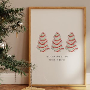 May include: A framed print featuring three watercolor Christmas trees with red ribbon accents. The trees are on a cream background, with the text "'Tis so sweet to trust in Jesus" below. The frame is a light wood color.