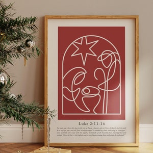 May include: A framed print featuring a minimalist white line drawing of a nativity scene on a red backdrop. The print, in a wooden frame, includes text from Luke 2:11-14. It's displayed near a decorated Christmas tree and wrapped gifts, evoking a festive atmosphere.