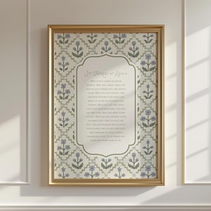 May include: A framed print with a gold-coloured frame. The print features a floral pattern in blue and green, surrounding a central text area with the words "St. Therese of Lisieux". The text is in a script font.