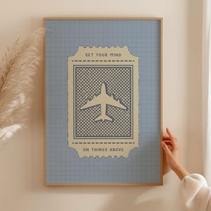 May include: A framed art print featuring a light blue background with a grid pattern. The print has a beige ticket-shaped design with an airplane graphic and the text "SET YOUR MIND ON THINGS ABOVE". The frame is a light brown color.