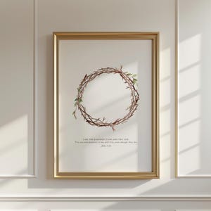 Könnte beinhalten: Ein gerahmter Druck mit einem goldenen Rahmen. Das Kunstwerk zeigt eine Aquarellillustration einer kreisförmigen Dornenkrone mit grünen Blättern. Der Text lautet: „ICH BIN DIE AUFERSTEHUNG UND DAS LEBEN. Wer an mich glaubt, wird leben, auch wenn er stirbt. Johannes 11:25.“